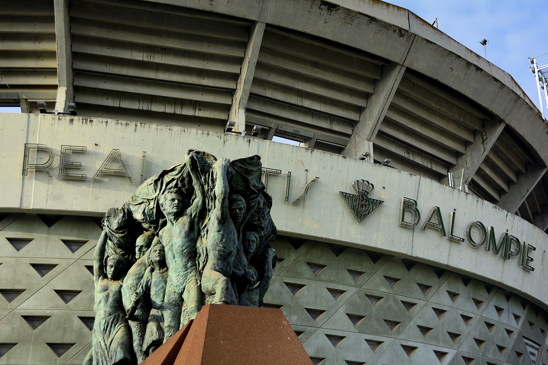 Vista de la fachada principal del Estadio Benito Villamarín, en primer plano un monumento en bronce situado en la esquina entre Avenida de la Palmera y…