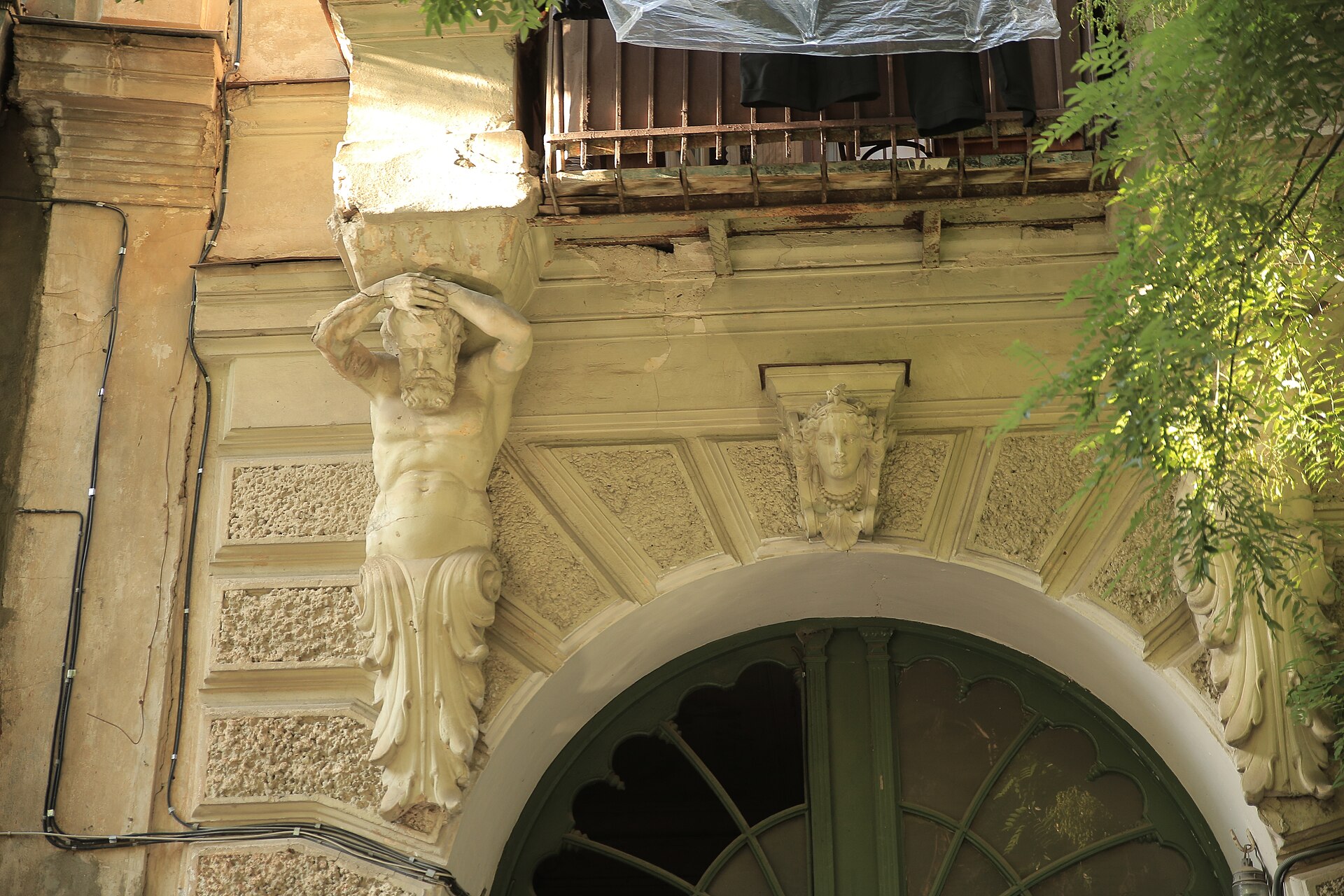 Architectural details of the entrance portal at 9 Gizo Nishnianidze Street, Sololaki, Tbilisi. The photograph shows an atlante, rusticated arch surround and a…