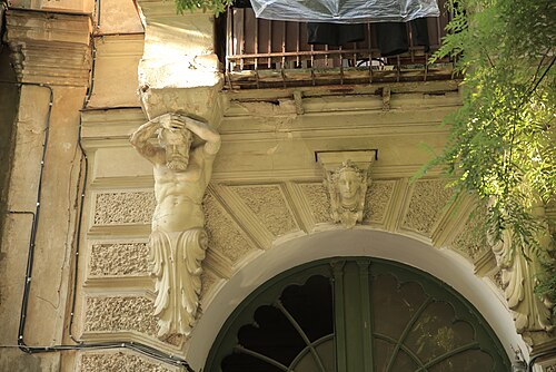 Architectural details of the entrance portal at 9 Gizo Nishnianidze Street, Sololaki, Tbilisi. The photograph shows an atlante, rusticated arch surround and a…